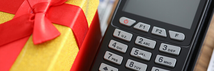 Close-up of terminal machine and yellow present box with red bow on top. Spending money on online shopping. Pay via credit card. Modern technology concept