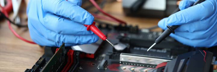 Close-up of middle-aged man measuring electrical voltage. Technician male repairing computer mainboard using digital multimeter. Technology and diy concept