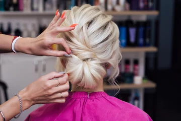 Gordijnen hairdresser makes his own hands hairstyle a bun on the head of a blonde girl © alexkoral