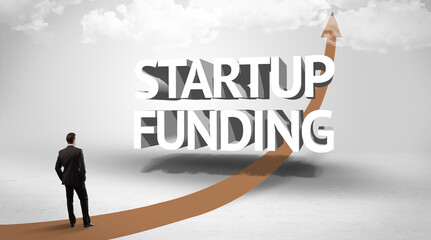 Fototapeta premium Rear view of a businessman standing in front of STARTUP FUNDING inscription, successful business concept