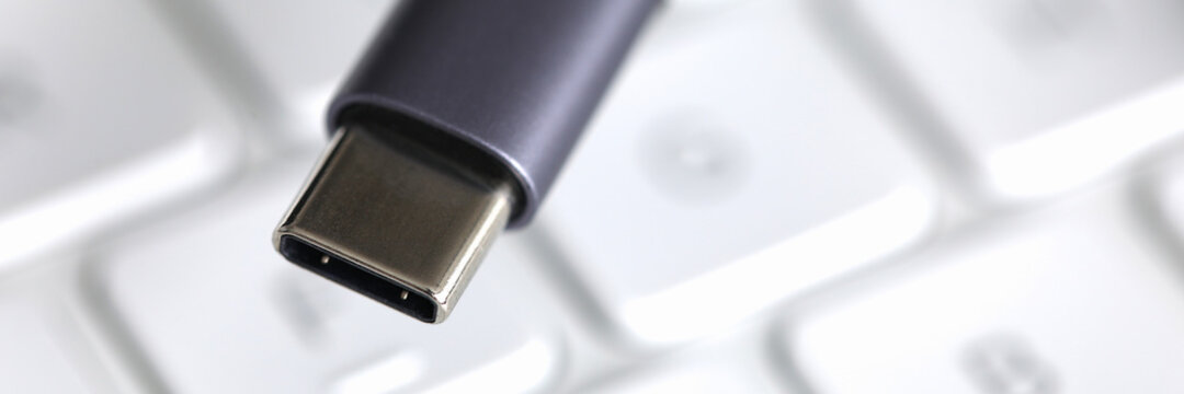 Close-up of black wire for connecting to device lies on white laptop keyboard. Computer accessories. Usb input for tablet. Modern technology and pc concept