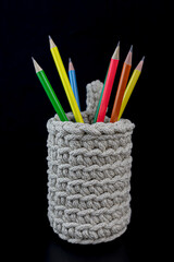 Needlework.Handmade items. Colored pencils in a knitted mug on a black background. Close-up elements