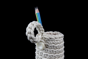 Needlework.Handmade items. Colored pencils in a knitted mug on a black background. Close-up elements