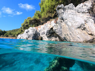 Fototapeta na wymiar Underwater and sea level photo of amazing tropical rocky turquoise clear seascape with caves and natural pine trees