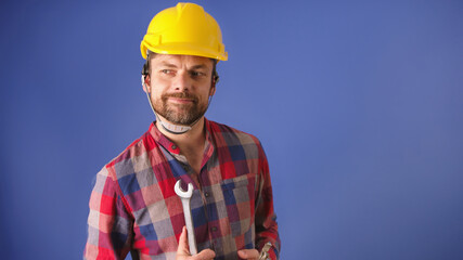 Portrait of the young man with yellow helmet and tools isolated on blue background. High quality photo