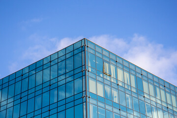 Fototapeta na wymiar Low angle view of modern office building covered with glass. Blue sky with some white clouds in the background. Corporate Buildings Theme.