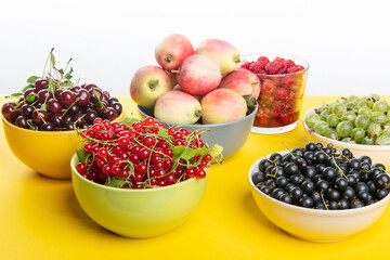 Fresh ripe vitamine berries and apples on yellow table: cherries, strawberries, gooseberries, redcurrant, blackcurrant