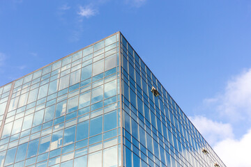 Obraz na płótnie Canvas Low angle view of modern office building covered with glass. Blue sky with some white clouds in the background. Corporate Buildings Theme.