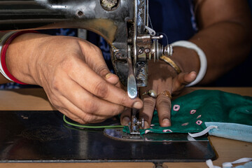 Indian woman working on old sewing machine, making homemade face masks against coronavirus or...