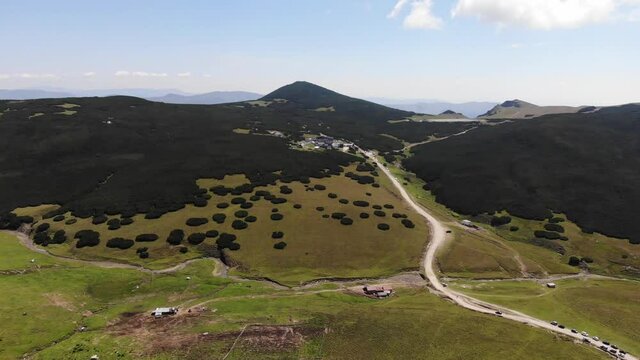 Reverse aerial shot of Piatra Arsa cabin and car park on a sunny day