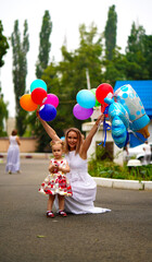 Mom in a white party dress with little baby holding beautiful balloons and toys