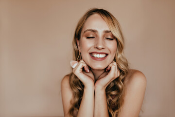 Refined european woman laughing with eyes closed. Indoor portrait of blissful blonde girl isolated...