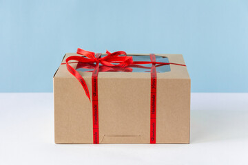 Present carton box with red tape and bow on blue background. Birthday gift concept.