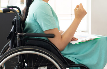 Obraz premium young asian disabled woman with smiling face sitting in the wheelchair and using computer to discuss project with her colleagues in the working office. disability and handicapped concept