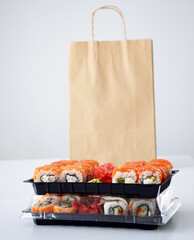 Set of various Philadelphia sushi rolls packed in plastic box for delivery near paper package with free place for text. Traditional Japanese cuisine. Take out food. Copy space. © Тетяна Немировська