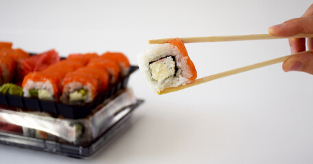 Philadelphia sushi in wooden sticks with set of various rolls in plastic box on baclground. Traditional Japanese food. Delivery service or take away concept.
