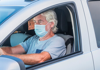 Attractive senior man driving his silver car wearing medical mask due to coronavirus happy for end lockdown at home
