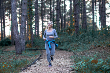 Aged woman jogging in park between woods at the end of day and smile