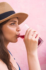 Fototapeta premium Beautiful blonde girl wearing makeup drinking wine in front of pick background in summer