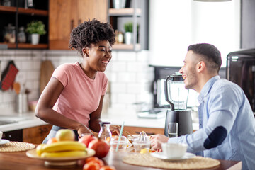 Obraz na płótnie Canvas Multiethnic couple in the kitchen preparing healthy smoothie