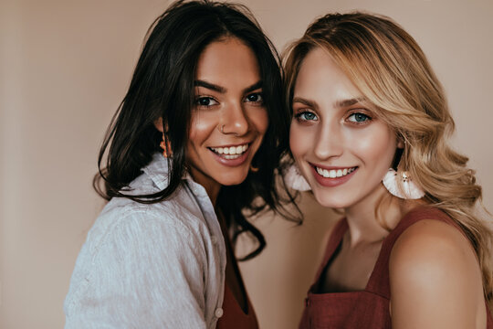 Close-up portrait of blue-eyed woman with makeup posing with friend. Indoor photo of smiling elegant girls.