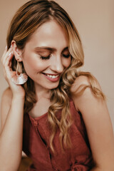 Fototapeta premium Glad female model in elegant earrings enjoying photoshoot. Studio close-up portrait of lovable european woman with blonde hair.