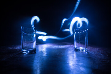Broken glasses on wooden table at dark toned background with fog. Selective focus