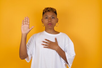 Young African American girl with afro short hair wearing white tshirt standing over isolated yellow...