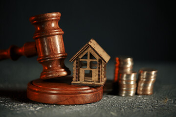 A row of coins on a small house model and a law auction hammer.