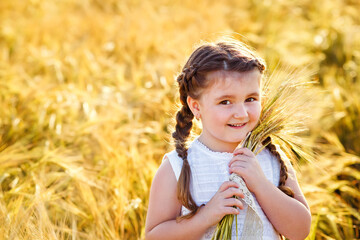 A happy girl in a white sundress stands on a field of ripe wheat in the rays of the setting sun. Wheat ear. Ears of rye. Selective focus. Setting sun. Walking through a field of rye.