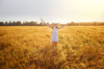 A happy girl in a white sundress jumps on a field of ripe wheat in the rays of the setting sun. Wheat ear. Ears of rye. Selective focus. Setting sun. Walking through a field of rye.