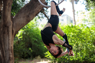 Aerial artist hanging from a hoop by her leg, in an acrobatic dance pose, dressed in matching black leggings and sleeves.