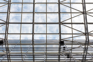 View from below on glass roof in building. Abstract background. Clouds on the sky are visible through glass.