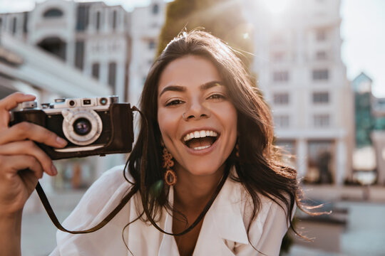 Enthusiastic female photographer looking to camera with pleased smile. Excited brunette girl with camera making photos.