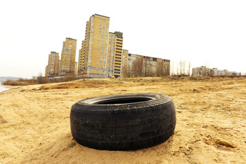 The car tire lies against the backdrop of city houses. Environmental pollution by law and order...