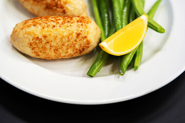 Breaded cutlet with green beans and lemon on a white plate. Close-up