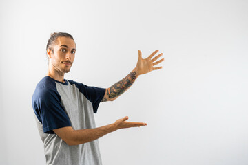 Hombre tatuado con pelo recogido y camiseta gris de mangas azules señala a un hueco en el que puedes poner tu texto o logo, en fondo blanco