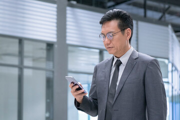 Fototapeta premium Chinese businessman in business suit and tie reading on his cellphone