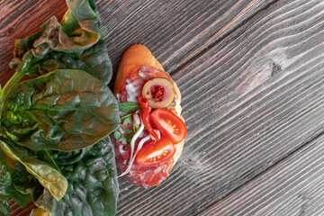 bruschetta with salami sausage, cherry tomatoes, olives, paprika, sprouts and spinach leaves nearby on the woodn background