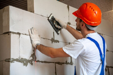 Mason aligning aerated autoclaved concrete block of constructed house wall