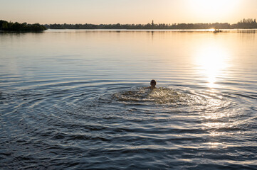 Swimming person with only the back of the head visible swimming in a lake at sunset.