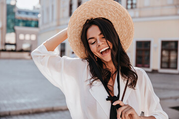 Gorgeous brunette woman wears white blouse smiling on street background. Beautiful laughing girl in...