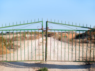 A wrought iron gate closed with a padlock in Spain. It is secured with a steel chain. Behind it is...