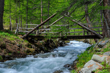 A small wooden bridge crosses a stream in the Hautes-Alpes. A motion blur effect is obtained by a slow shutter adjustment.