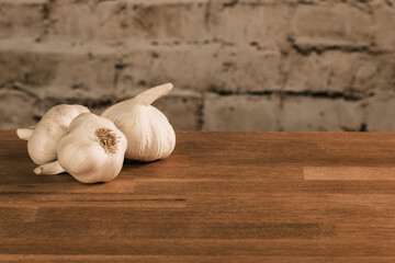 Mehrere Knollen von Knoblauch / Knoblauchzwiebeln auf einem Holztisch vor einer Stein-Mauer im Hintergrund