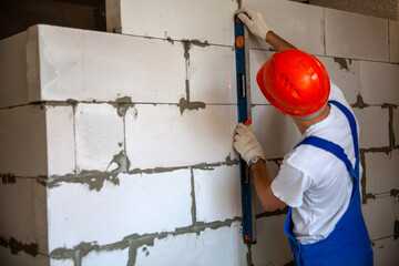 Mason aligning aerated autoclaved concrete block of constructed house wall