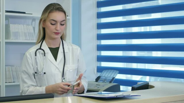 Pretty nurse using tablet and phone at hospital reception desk
