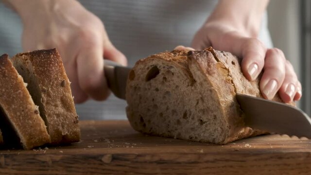 Slow motion of woman's hands cutting bread. Sourdough wholewheat bread cut in slices