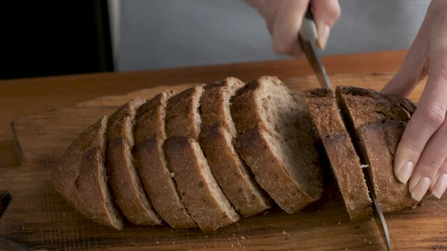 Woman cutting bread in slices. Sourdough whole wheat bread cut. Cooking process. 4K footage