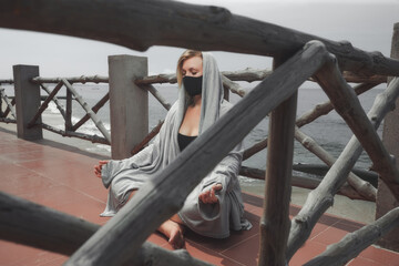Woman with black face protective mask  in lotus pose in the beach.
